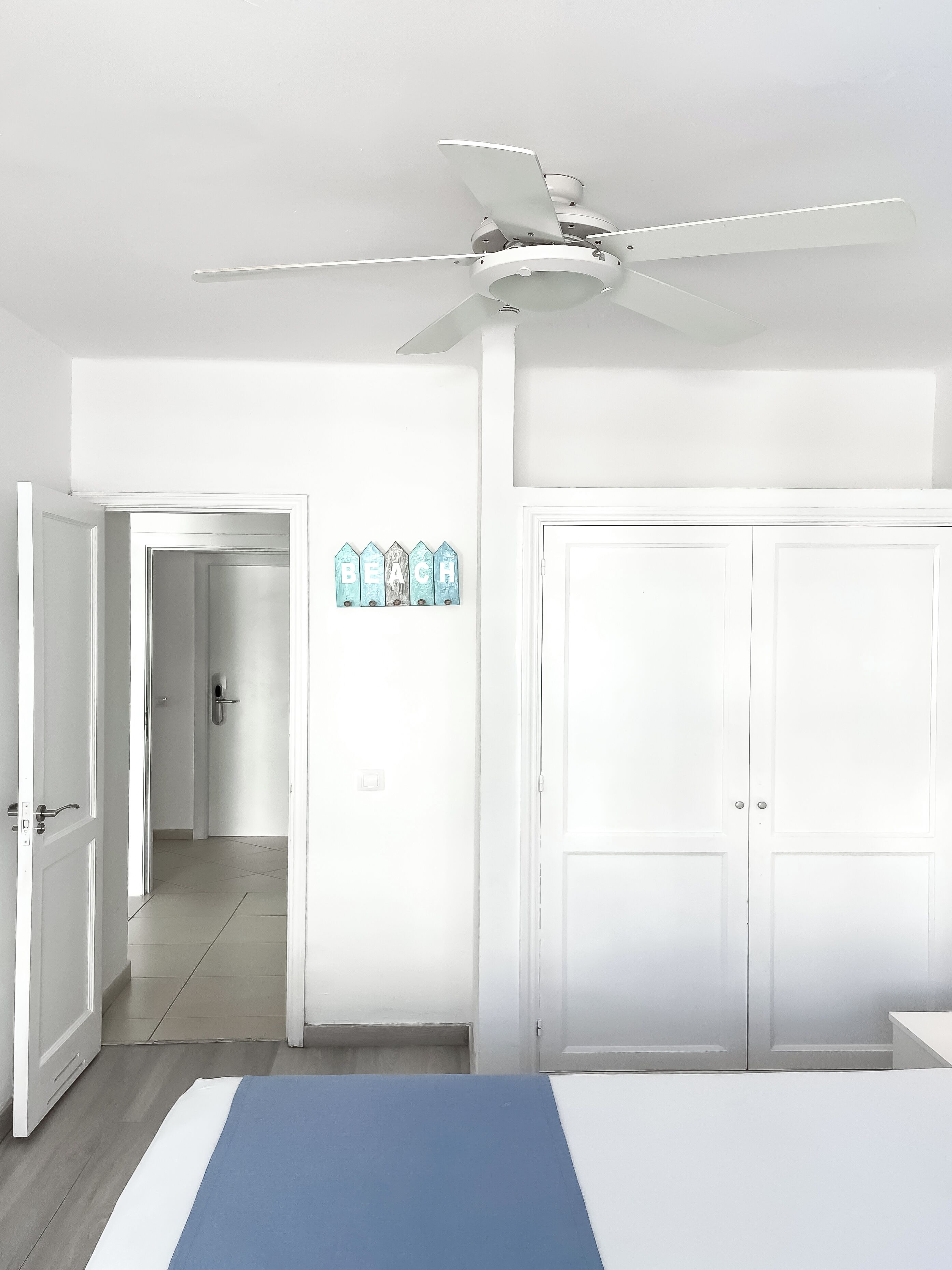 A bedroom with a bed, a ceiling fan, a wardrobe, and a hallway leading to another room.
