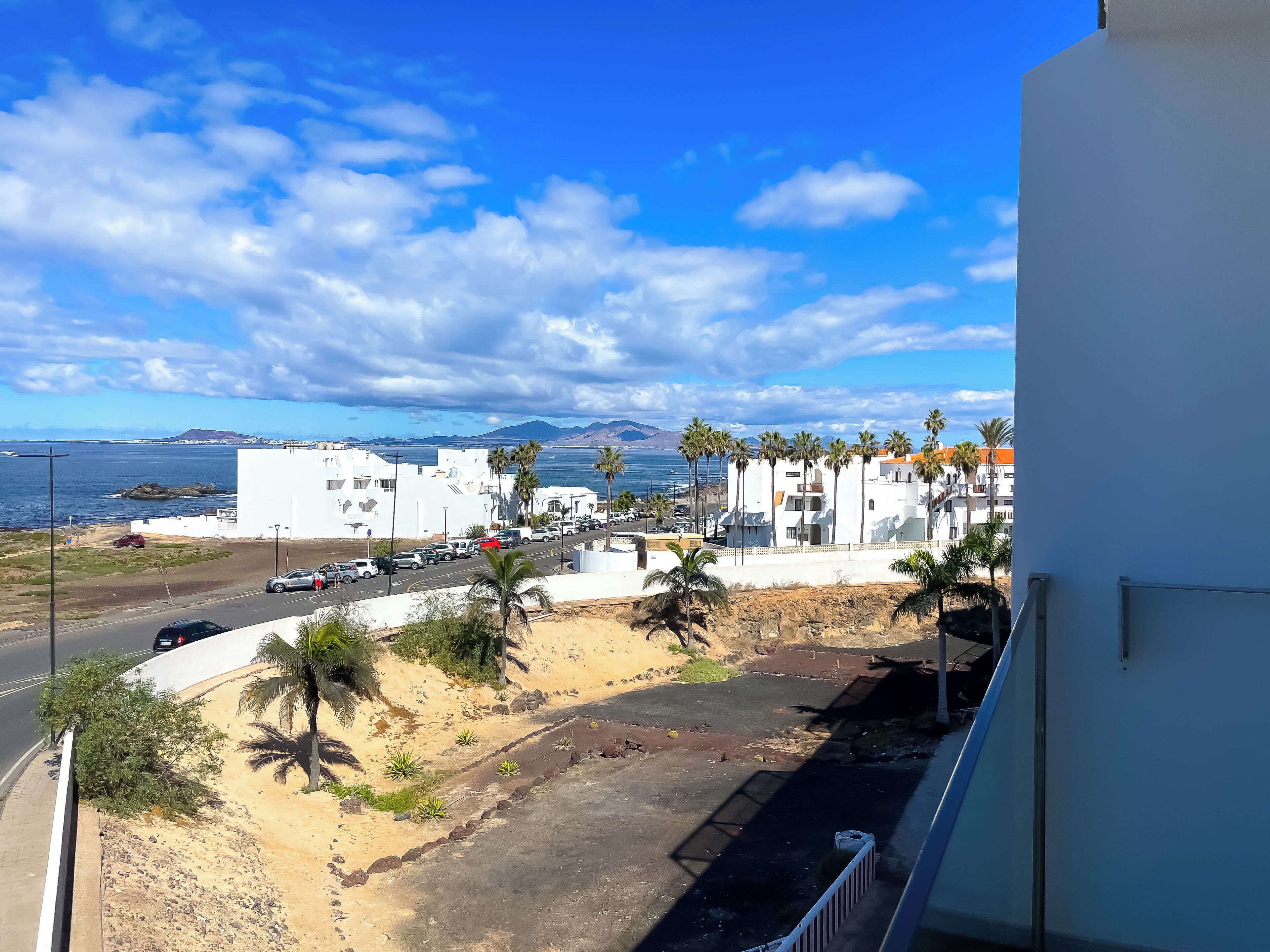 Blick auf die Küste mit weißen Gebäuden, Palmen und einer Straße, die zum Strand führt.