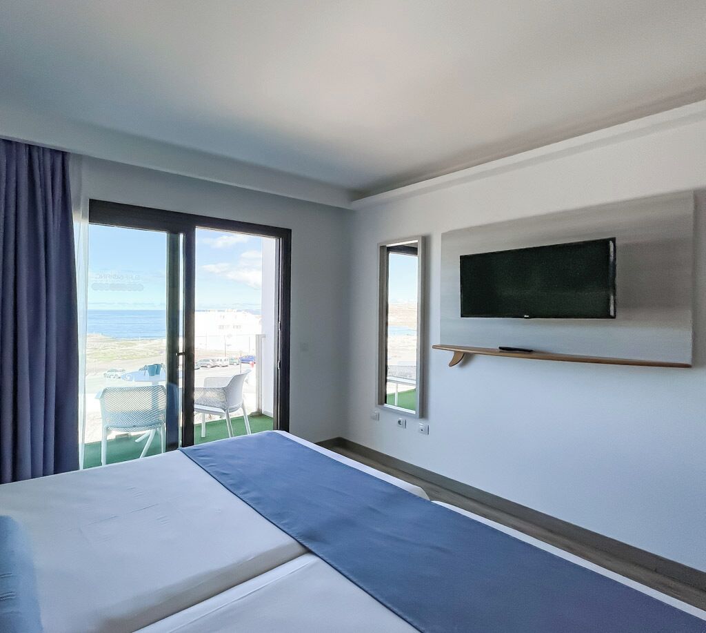 Une chambre d’hôtel avec un lit, un téléviseur fixé au mur et un balcon donnant sur la mer.