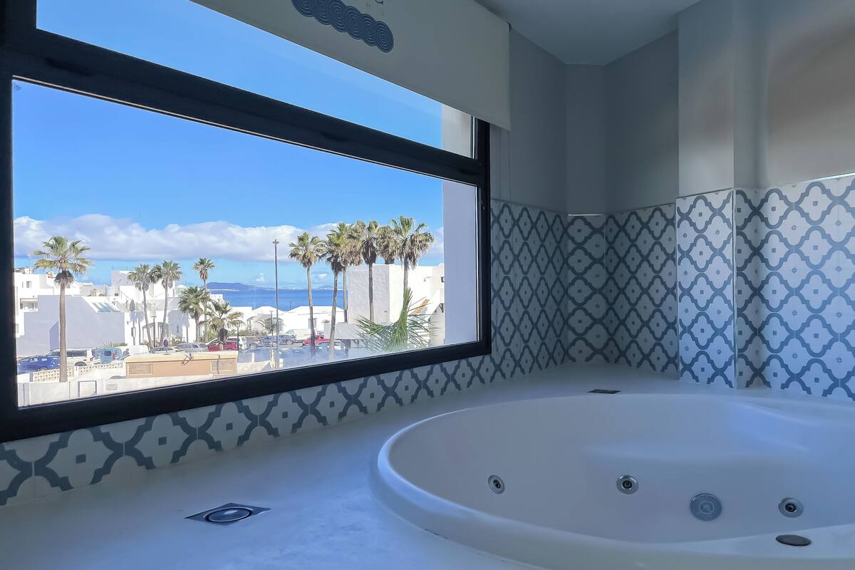 A bathroom with a large window, a bathtub, and patterned tiles.