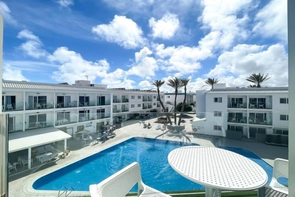 A hotel with a swimming pool, outdoor seating, and palm trees.