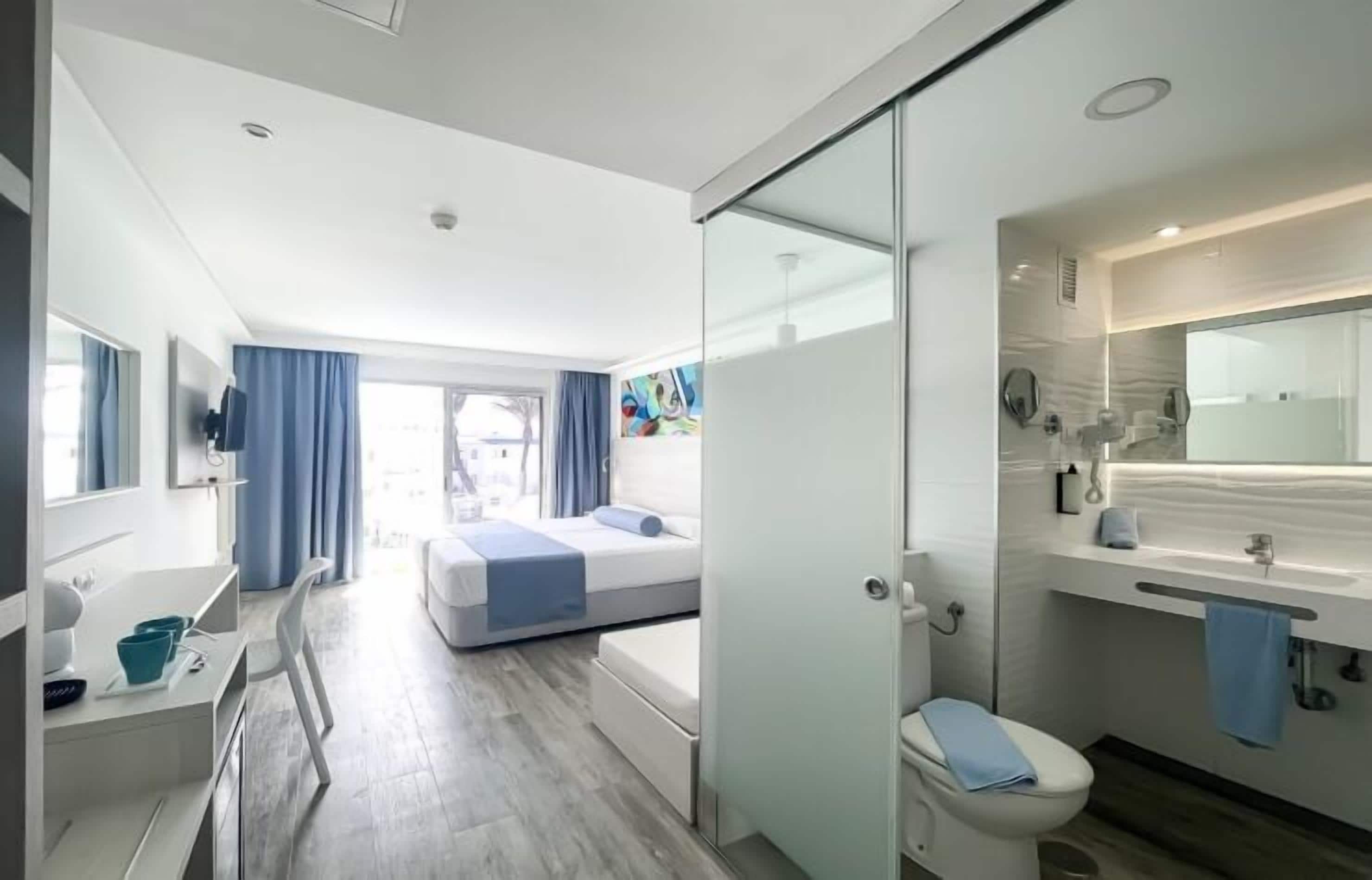 A modern hotel room with a bed, a bathroom, and a desk with a chair.
