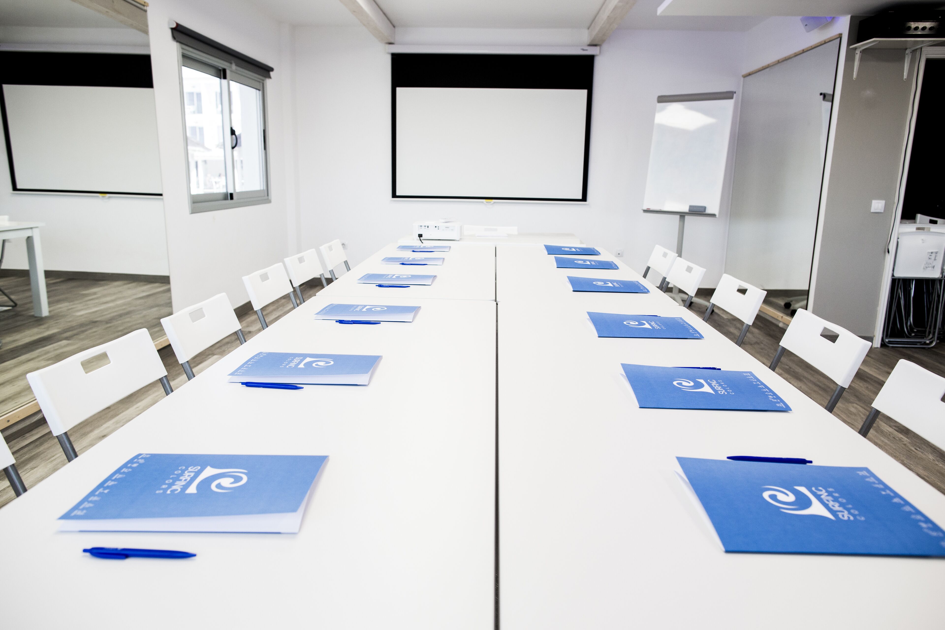 A conference room with white tables, blue folders, and white chairs.