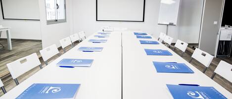 A conference room with white tables, blue folders, and white chairs.