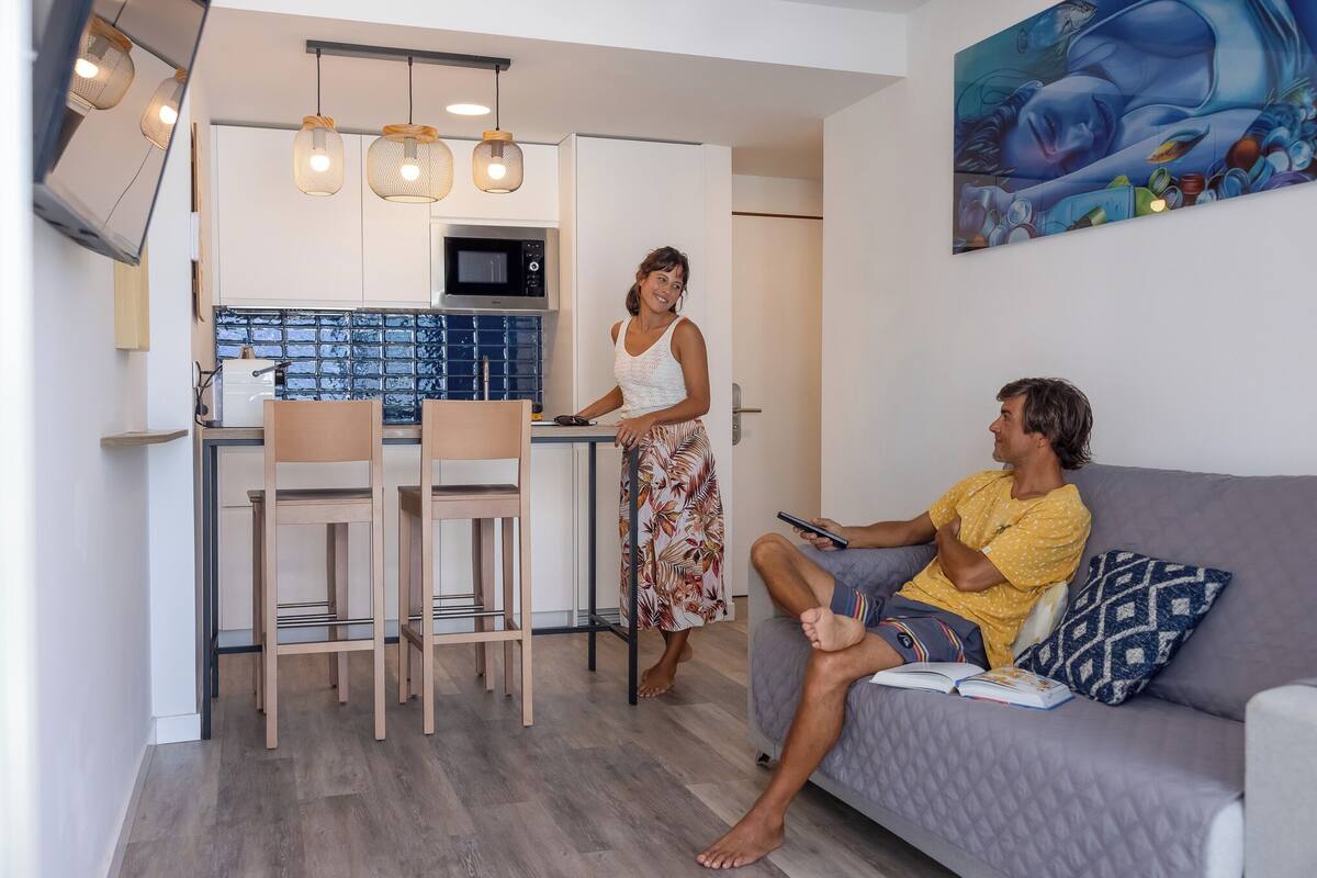 A modern kitchen with a microwave, a dining area with chairs, and a living room with a sofa and a painting on the wall.