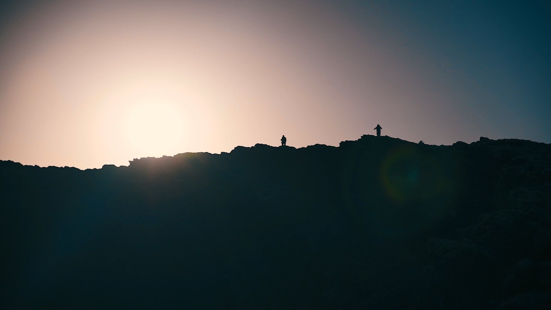La silhouette d’une personne se tenant sur une colline, avec le soleil en arrière-plan.