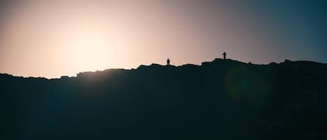 Eine Silhouette einer Person, die auf einem Hügel steht, mit der Sonne im Hintergrund.