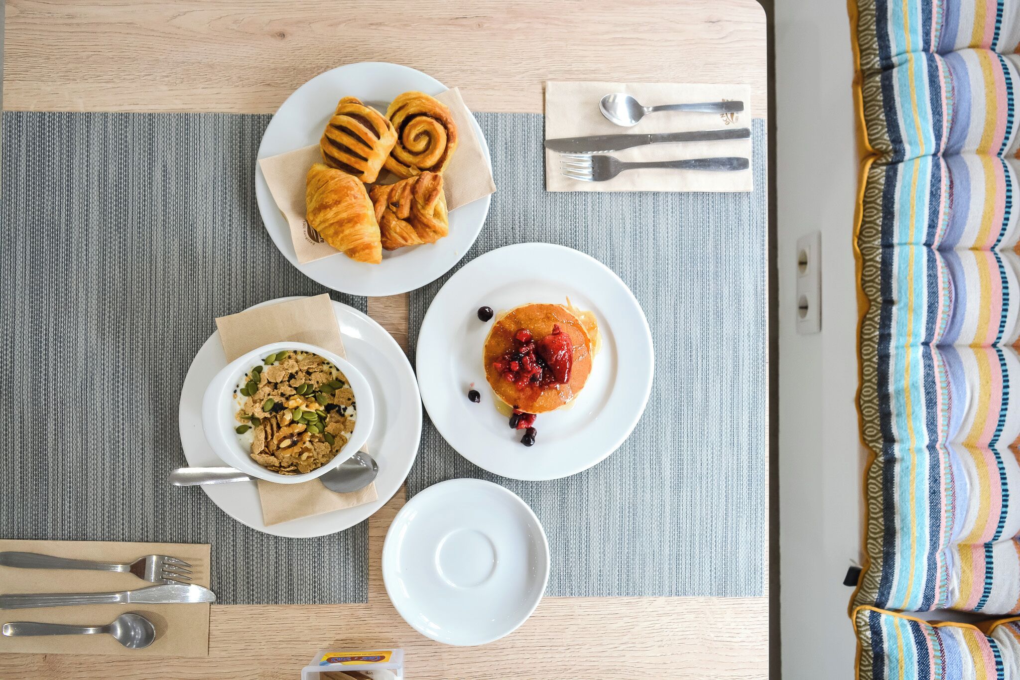 A breakfast setting with croissants, pancakes with berries, and cereal on a table with a striped placemat.