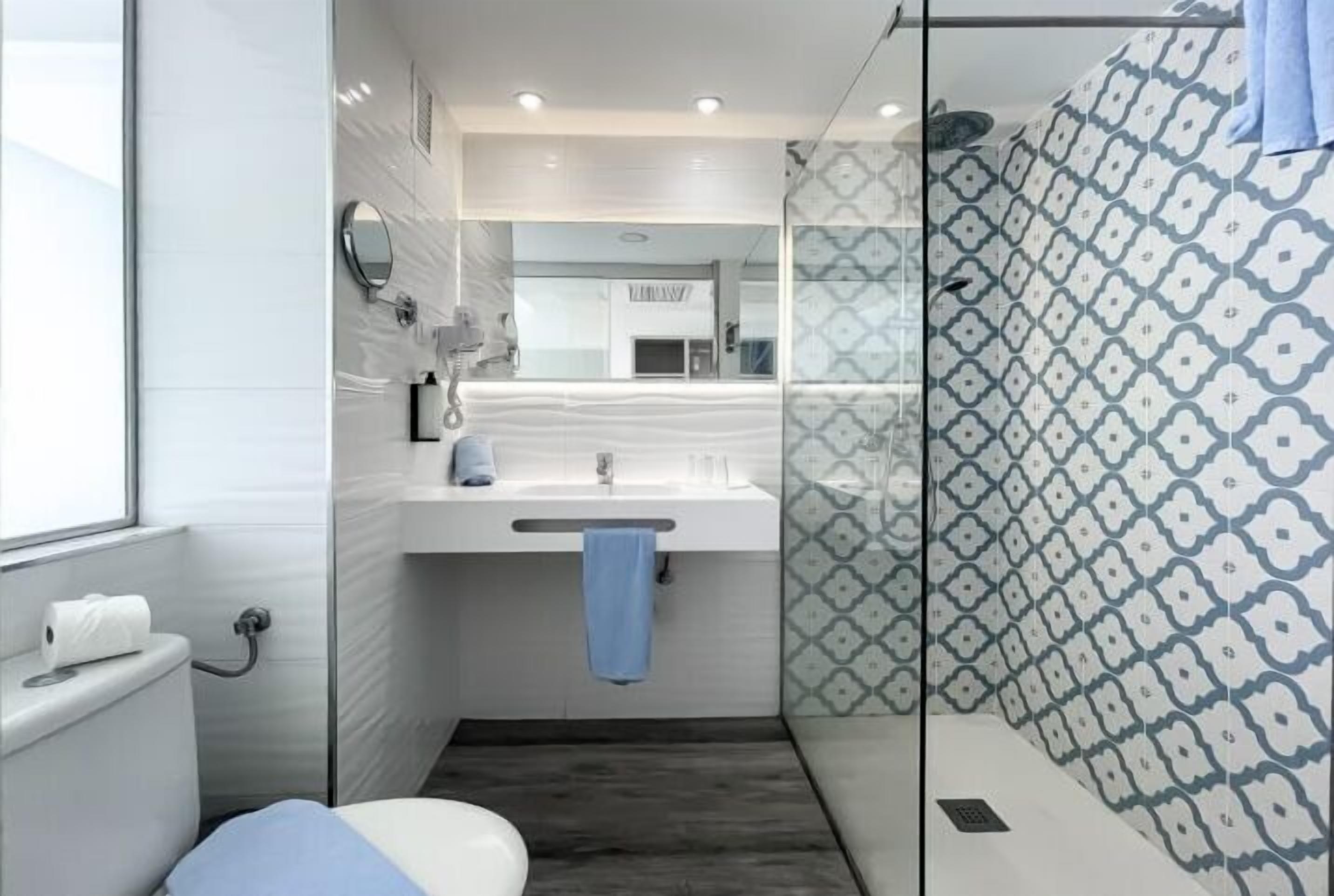 A modern bathroom with a glass shower enclosure, a white sink with a towel, and a toilet.