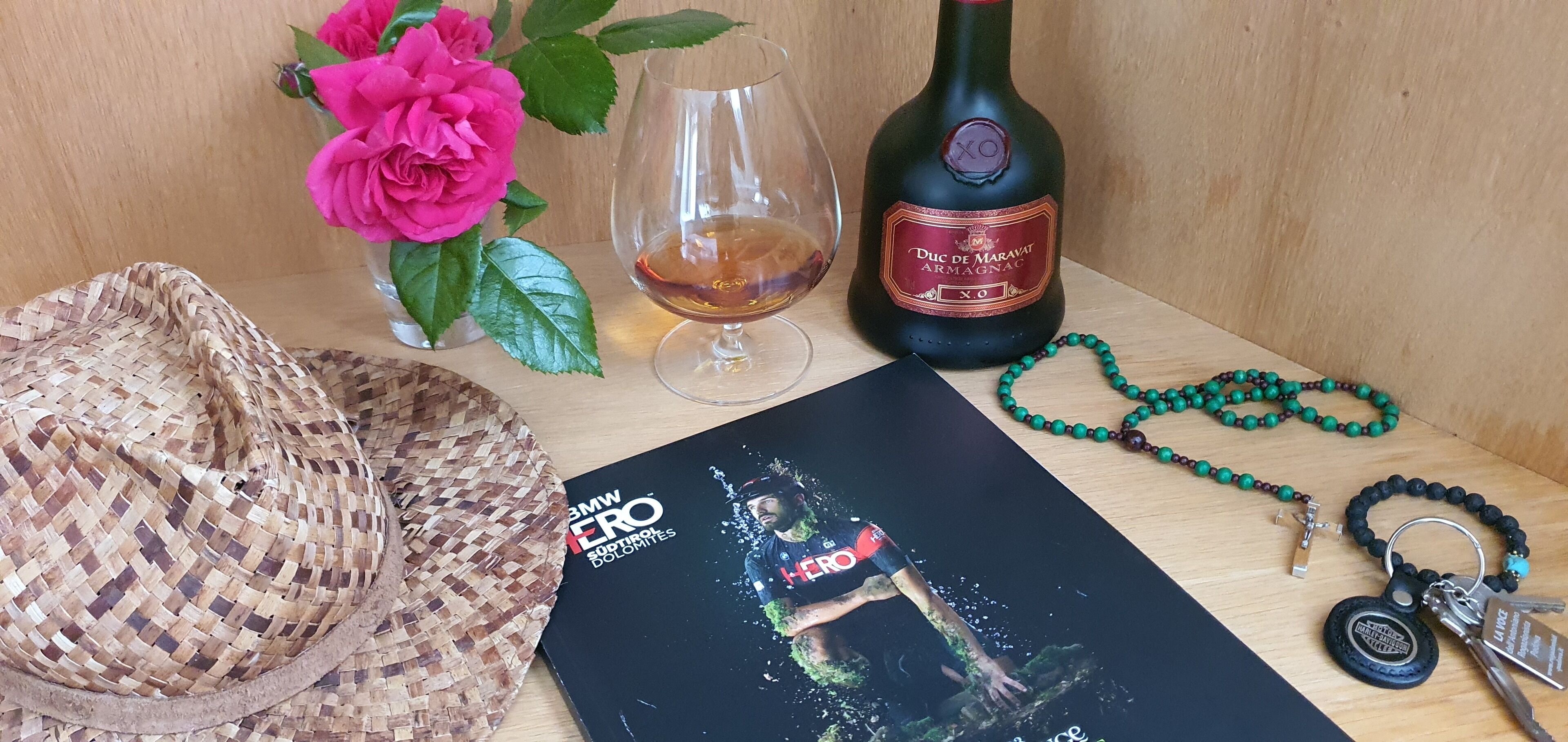 Una mesa de madera con una botella de vino, una copa, una cesta tejida, un libro y un rosario.
