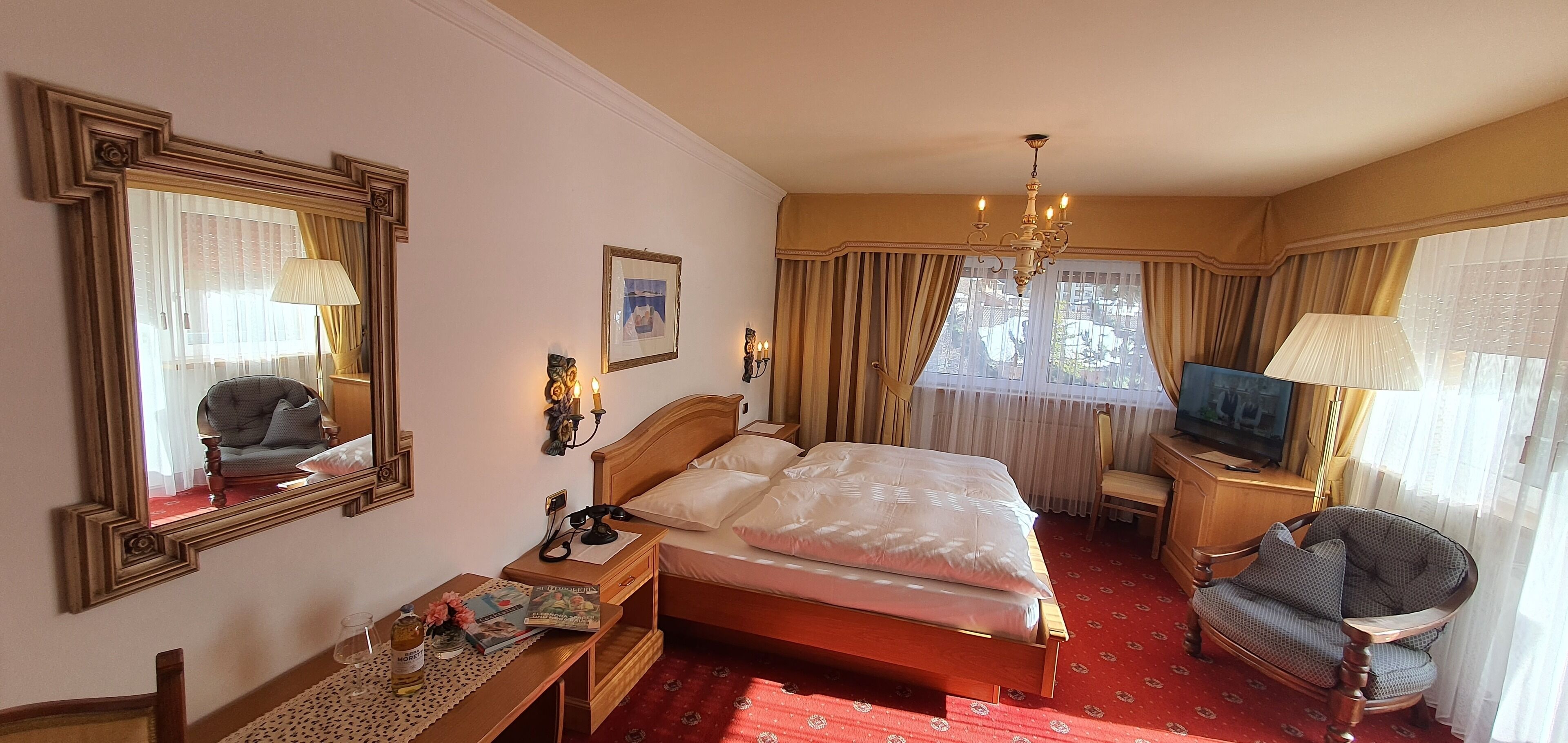 Habitación de hotel con una cama grande, un escritorio con lámpara, una silla, televisor y una ventana con cortinas.