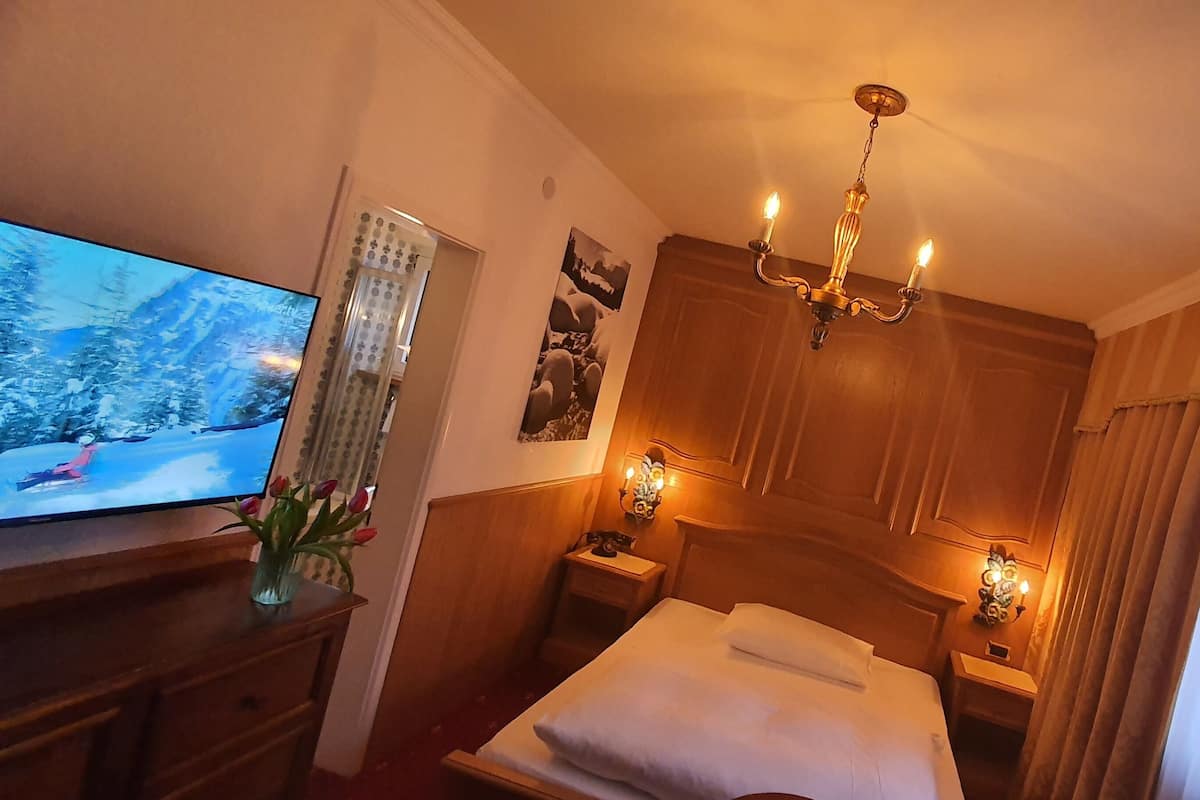 Ein Hotelzimmer mit einem Bett, einem Fernseher auf einer Holzkommode, einer Kristallleuchtre und einem Vorhangfenster.