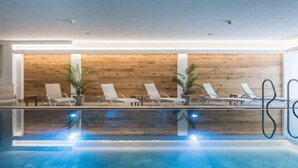An indoor swimming pool with lounge chairs and wooden panel walls. - Hotel Kertess (Sankt Anton am Arlberg)