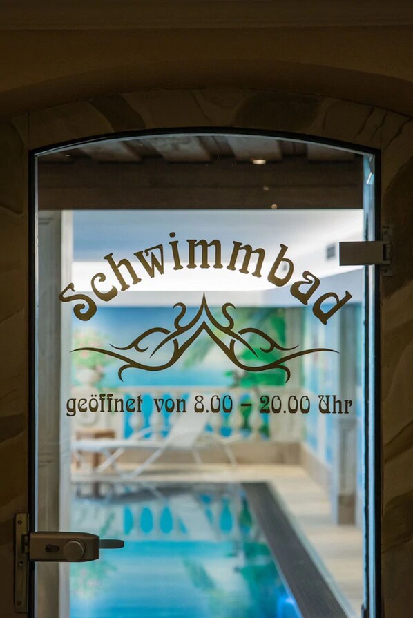 A glass door with the text "Schwimmbad" and operating hours. - Hotel Kertess (Sankt Anton am Arlberg)