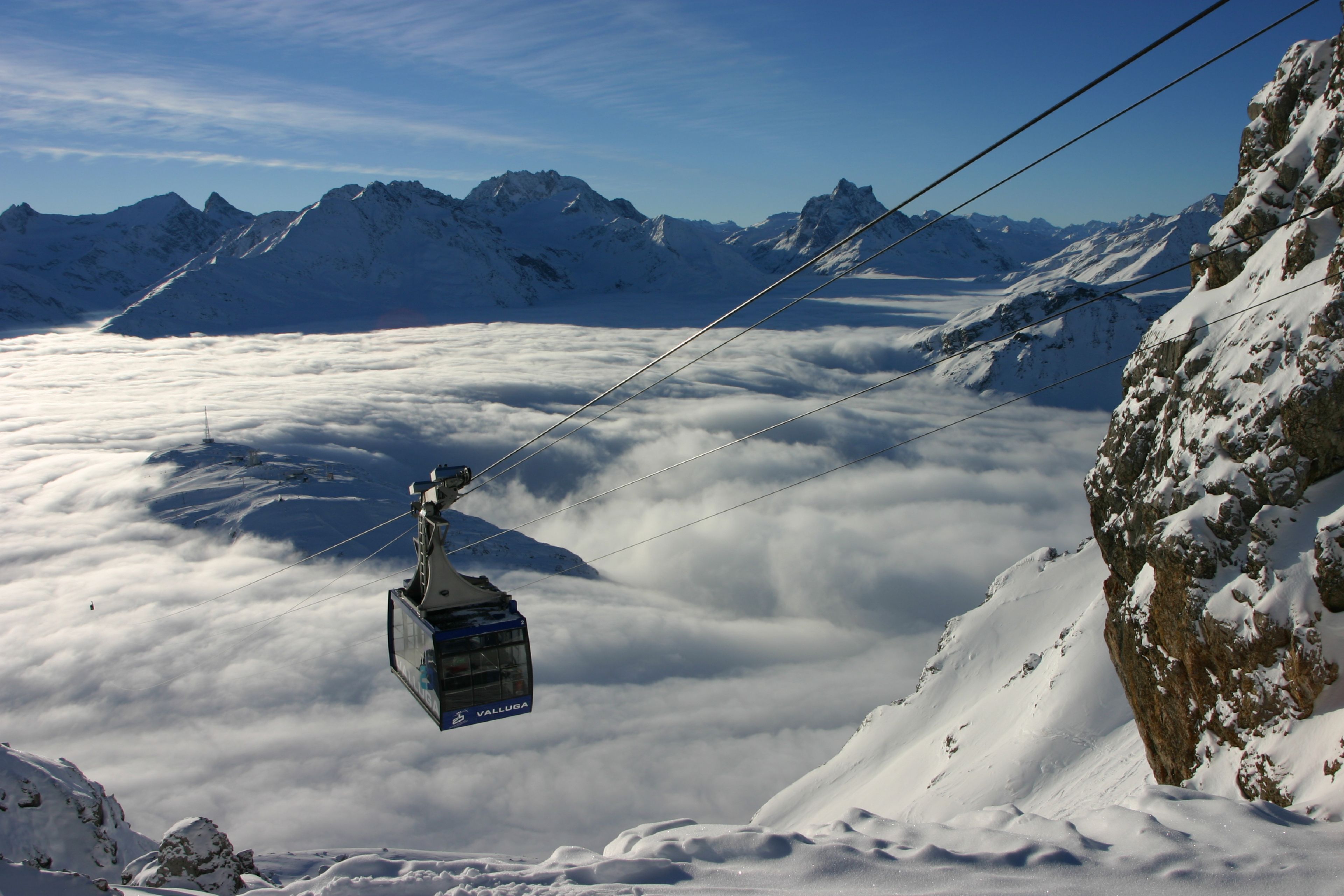 Een kabelbaan rijdt over een besneeuwd berglandschap met een heldere lucht.