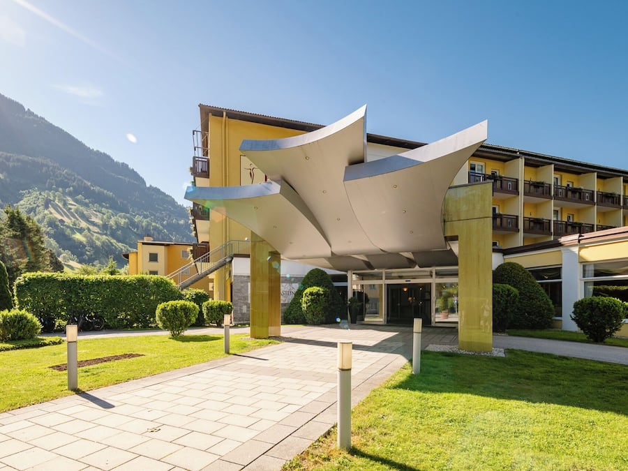 Un hotel con un diseño arquitectónico moderno, que destaca por una estructura sobresaliente y un telón de fondo montañoso.