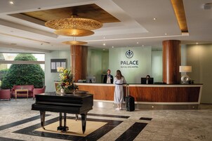 Zona de recepción de hotel con mostrador, un piano y una gran araña.