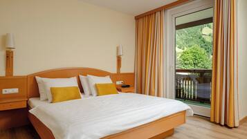 A hotel room with a large bed, a nightstand, a lamp, and a view of a balcony with curtains.