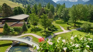 Un paisaje montañoso con un puente, senderos y un edificio de techo inclinado.