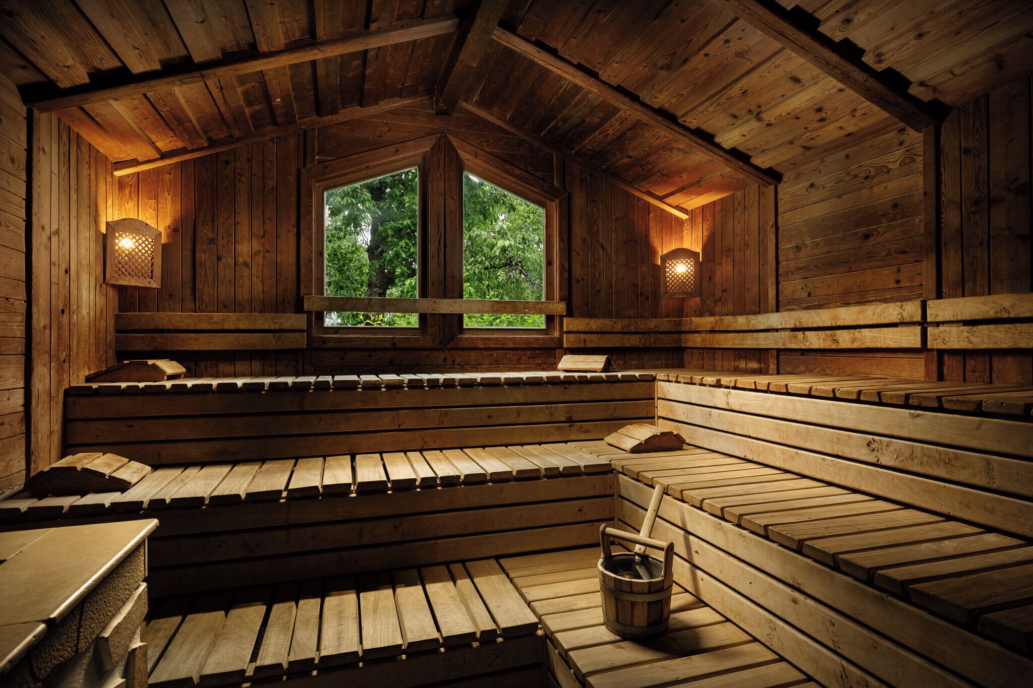 A wooden sauna with benches and a window, and a bucket on the floor.