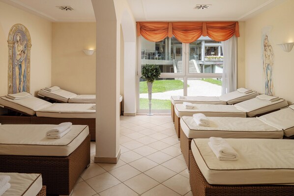 A spa room with multiple massage tables, a large window with curtains, and a view of a building outside.
