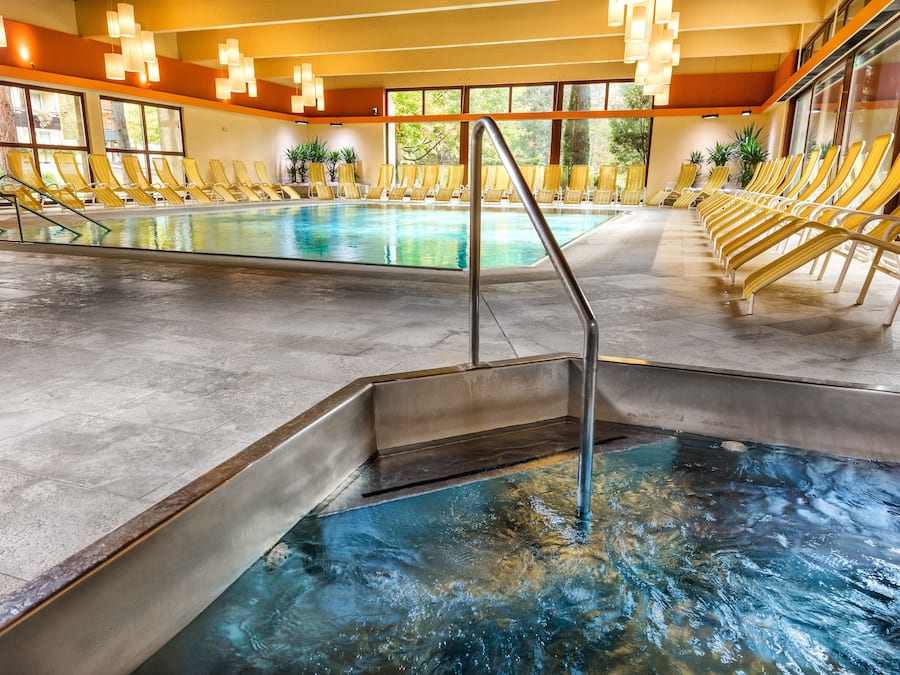Una piscina interior con sillas reclinables amarillas y una vista despejada del exterior a través de amplios ventanales.