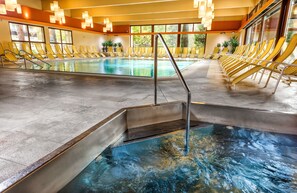 An indoor swimming pool with yellow lounge chairs and a clear view of the outdoors through large windows.