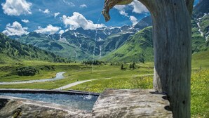 Una estructura de madera rústica con un arroyo que serpentea por un valle, rodeado de montañas y vegetación.