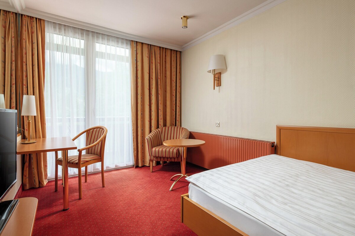 A hotel room with a bed, a desk, a chair, a television, and a window with curtains.