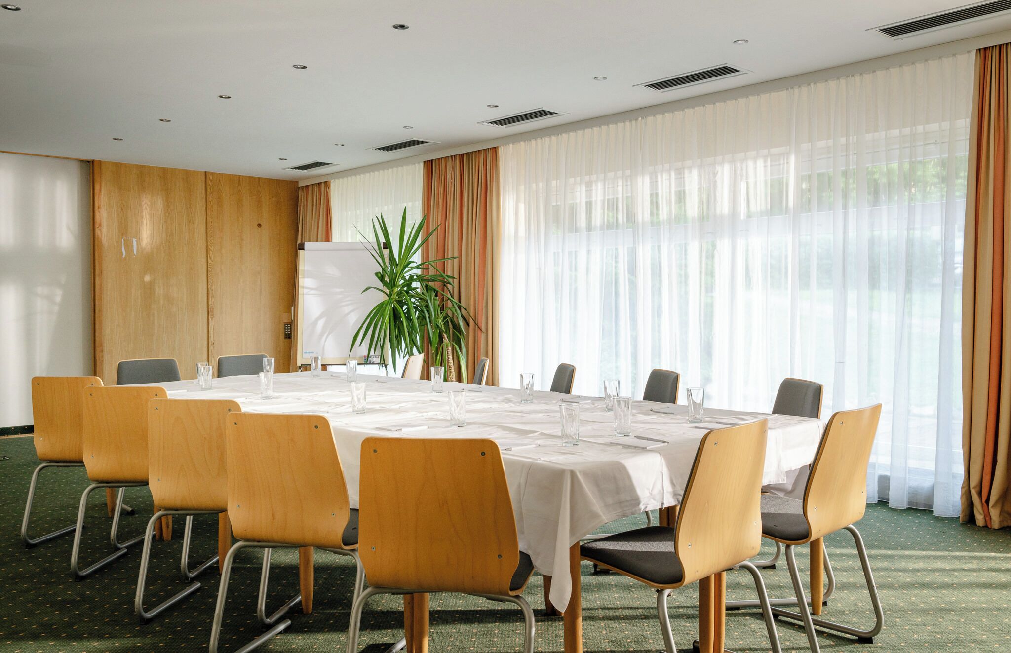 A conference room with a round table, chairs, a whiteboard, and a potted plant.