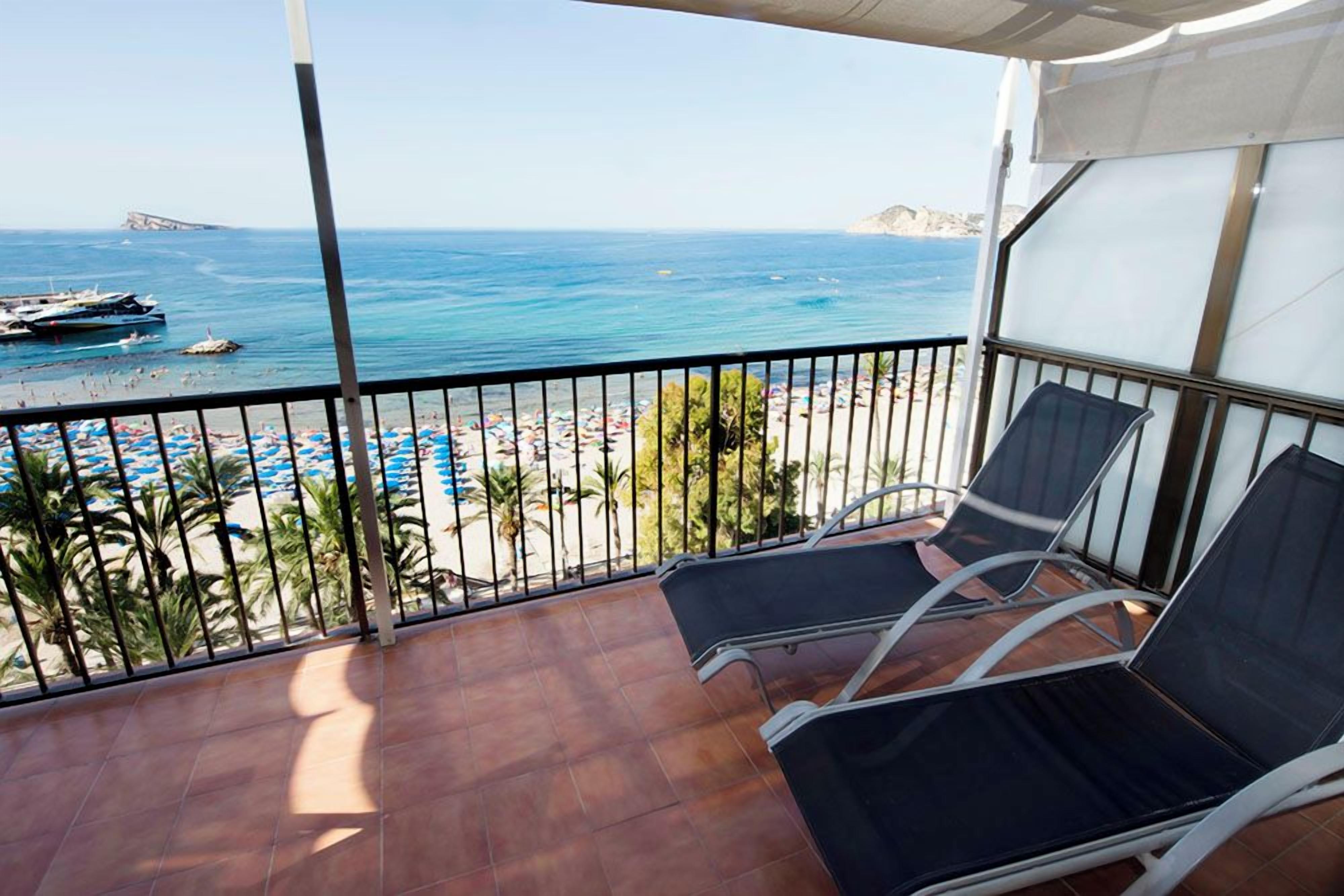 En balkon med to liggestole, havudsigt og en strand med parasoller.