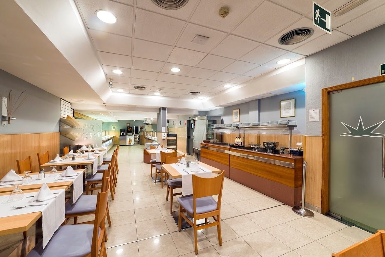 Um restaurante com várias mesas e cadeiras, um balcão com alimentos à mostra e um sinal de banheiro na parede.