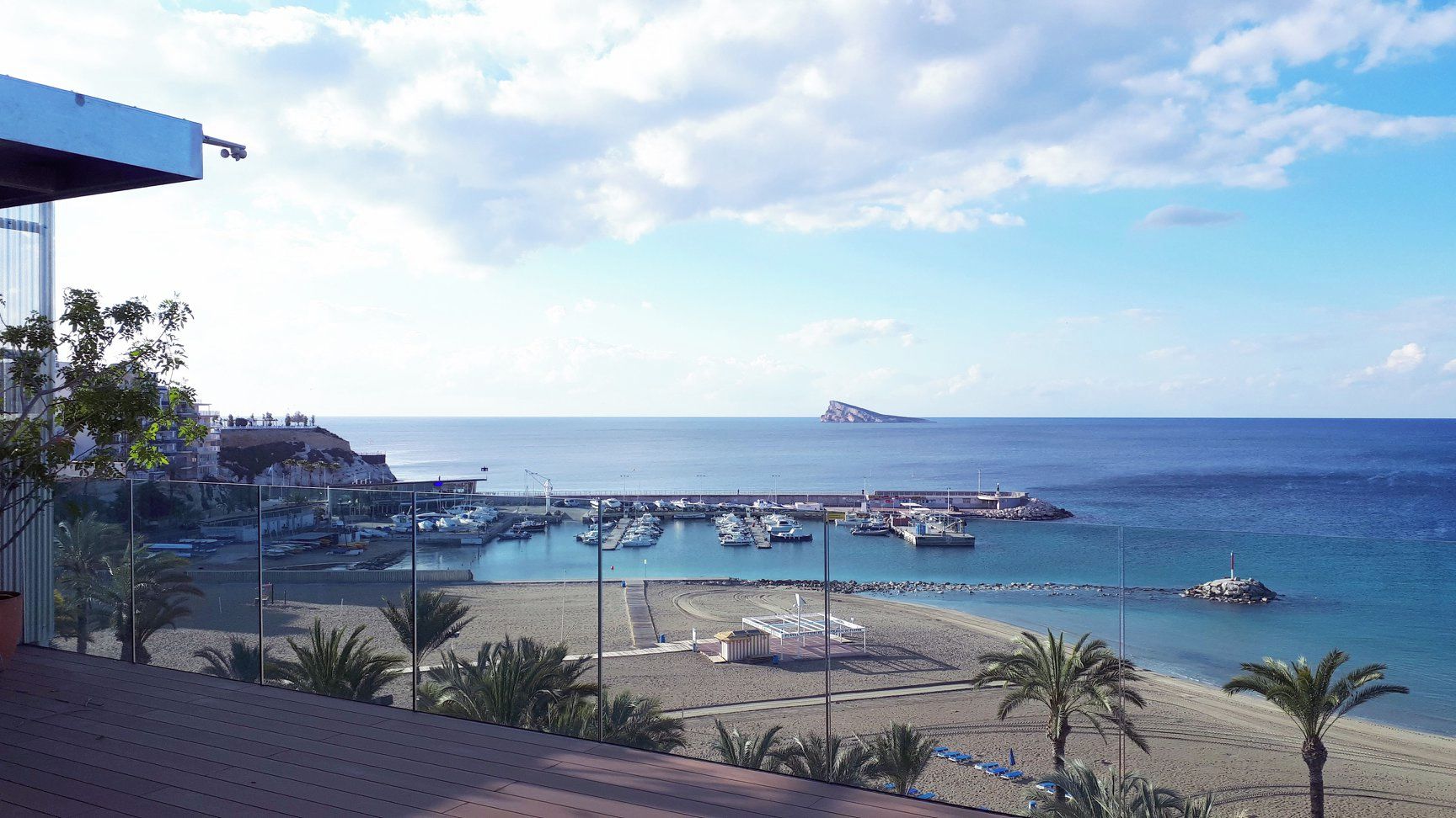 A coastal marina with boats docked, a beach, and a rocky outcrop in the distance.