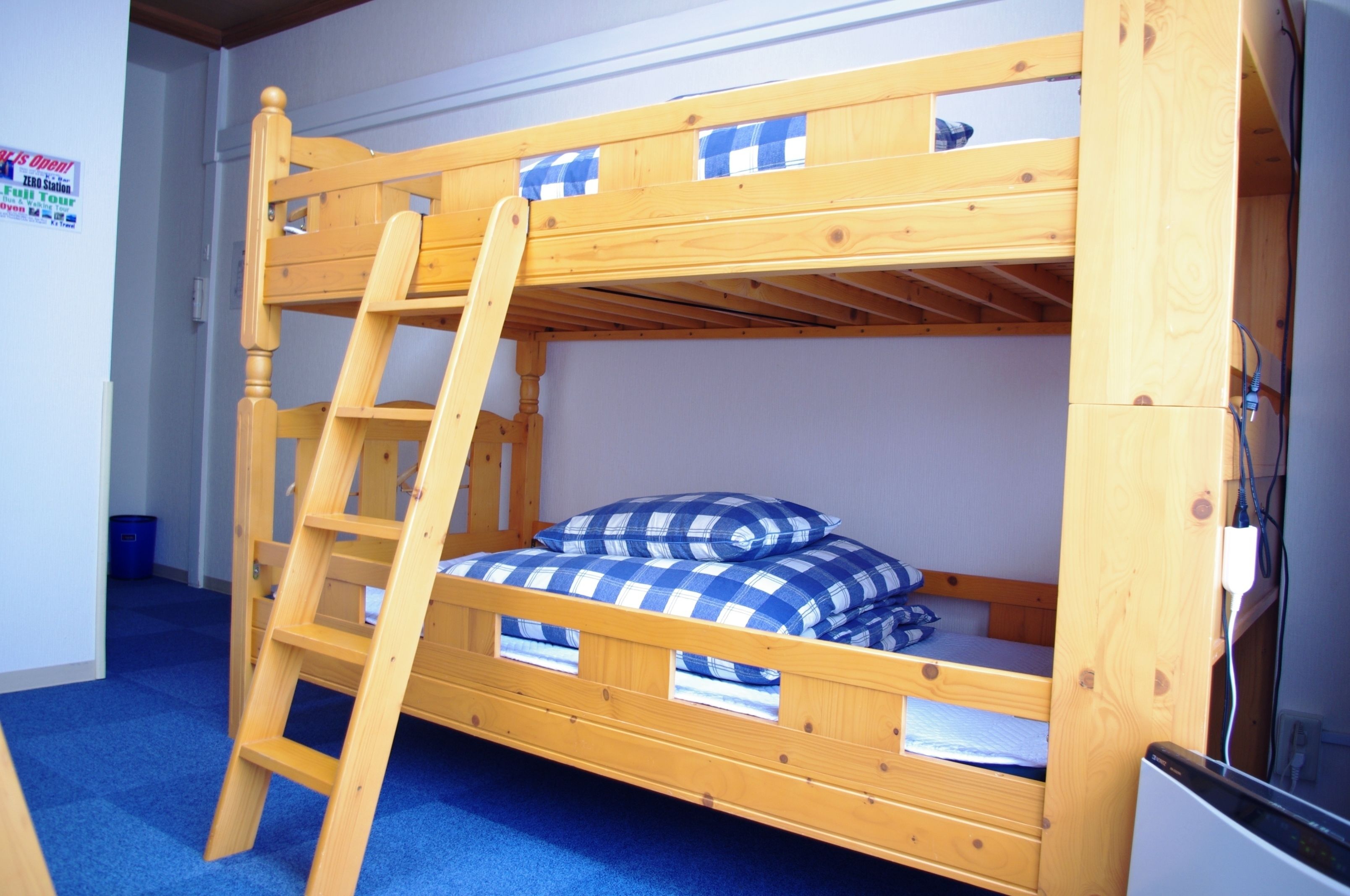 A bunk bed with a wooden ladder, a blue and white checkered blanket, and a small desk with a chair.