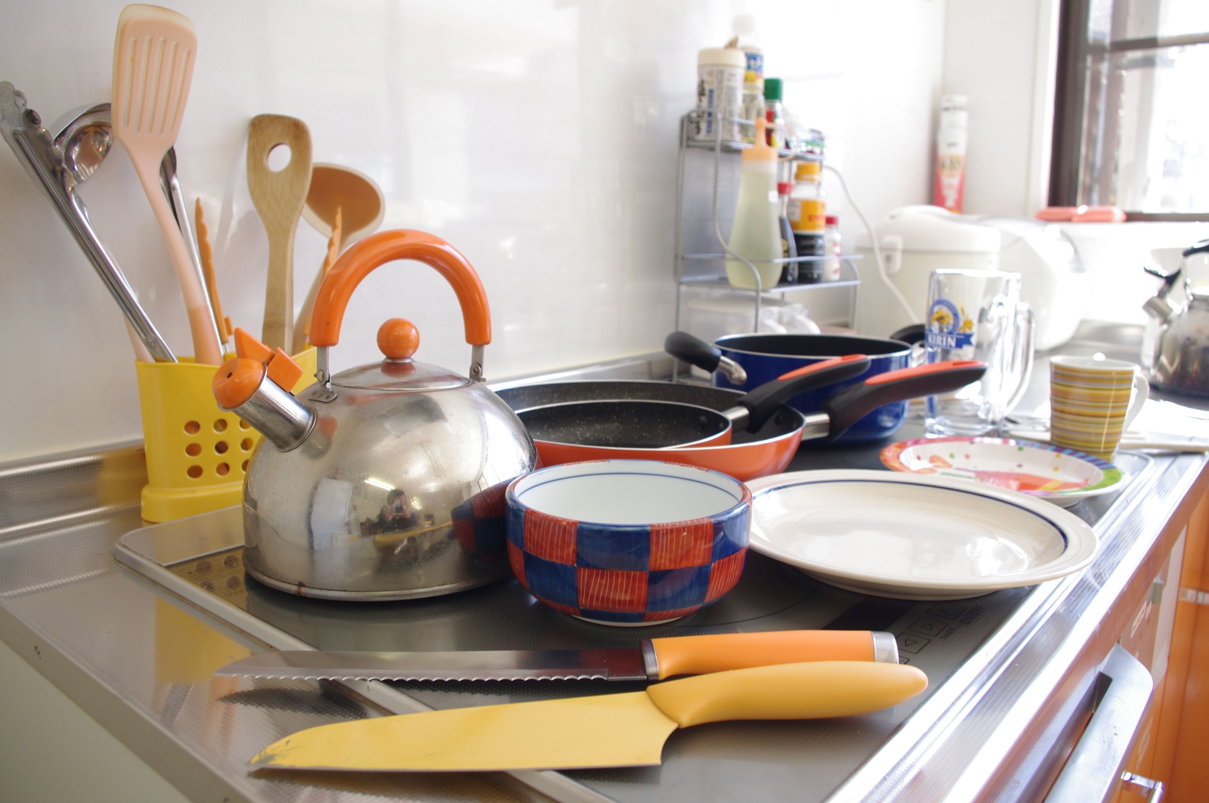 A kitchen counter with various utensils, cookware, and dishes.