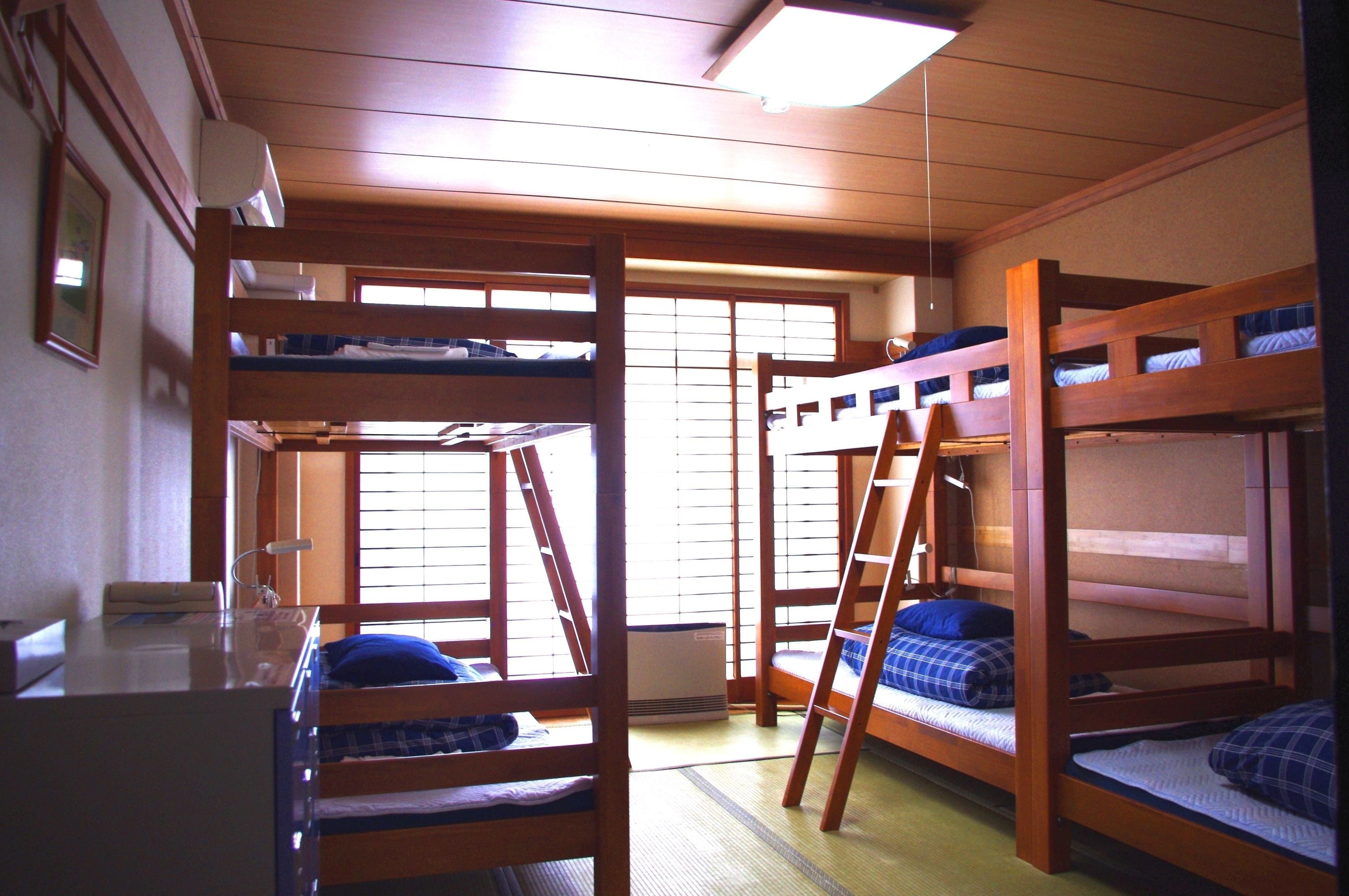 A dormitory room with bunk beds, a desk, and a window.