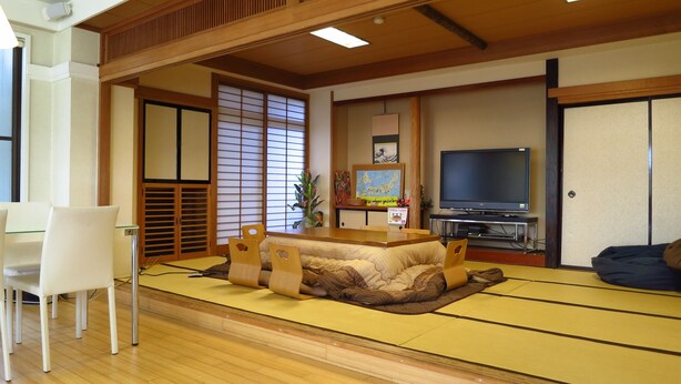 Un salon de style japonais traditionnel, avec un sol recouvert de tatamis, une basse table en bois, un téléviseur et une porte coulissante.