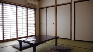 Une pièce de style japonais traditionnel, avec un sol recouvert de tatamis, des portes coulissantes et une petite table basse entourée de coussins.