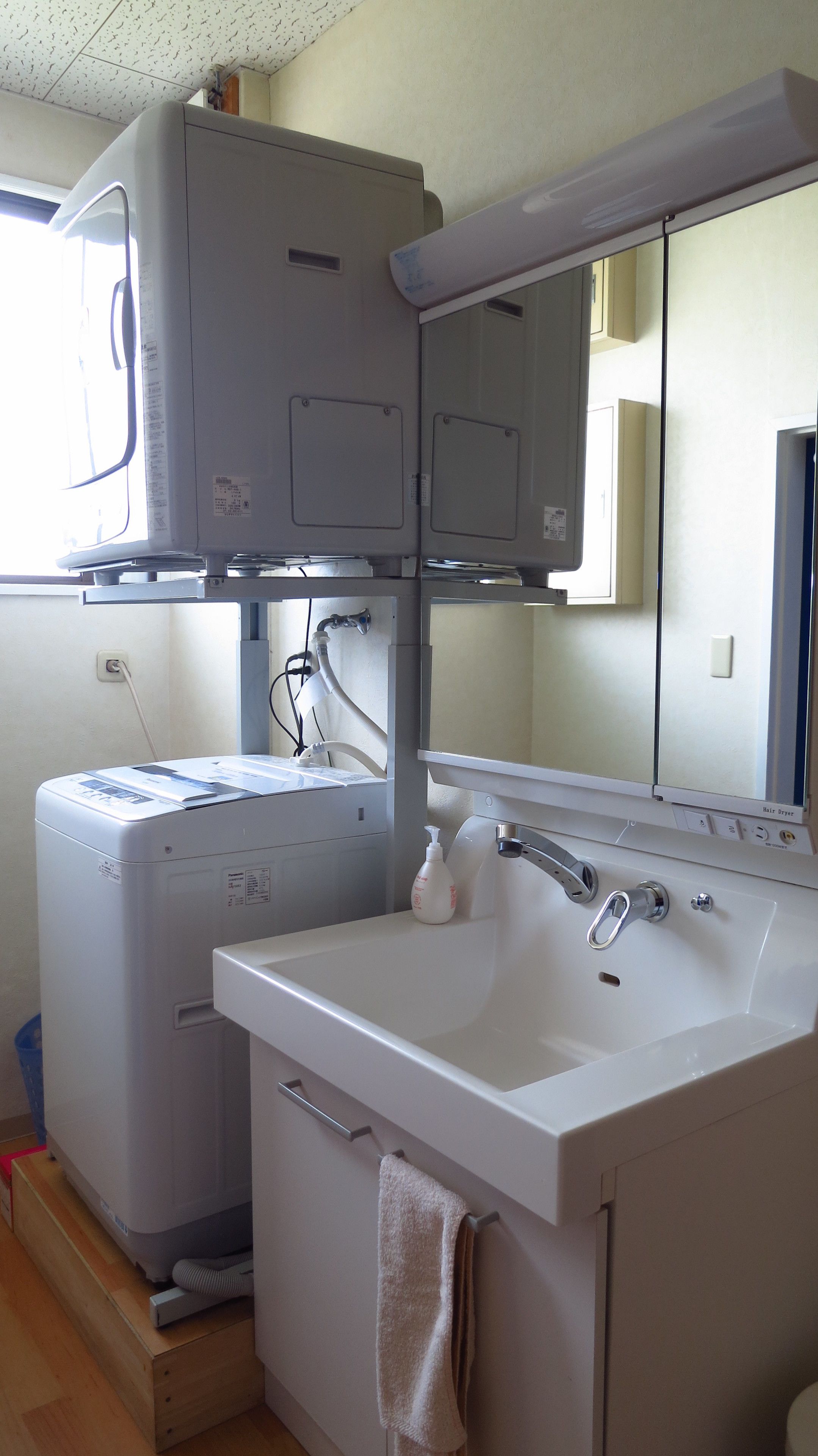 A compact bathroom with a washing machine, a sink, and a mirror.