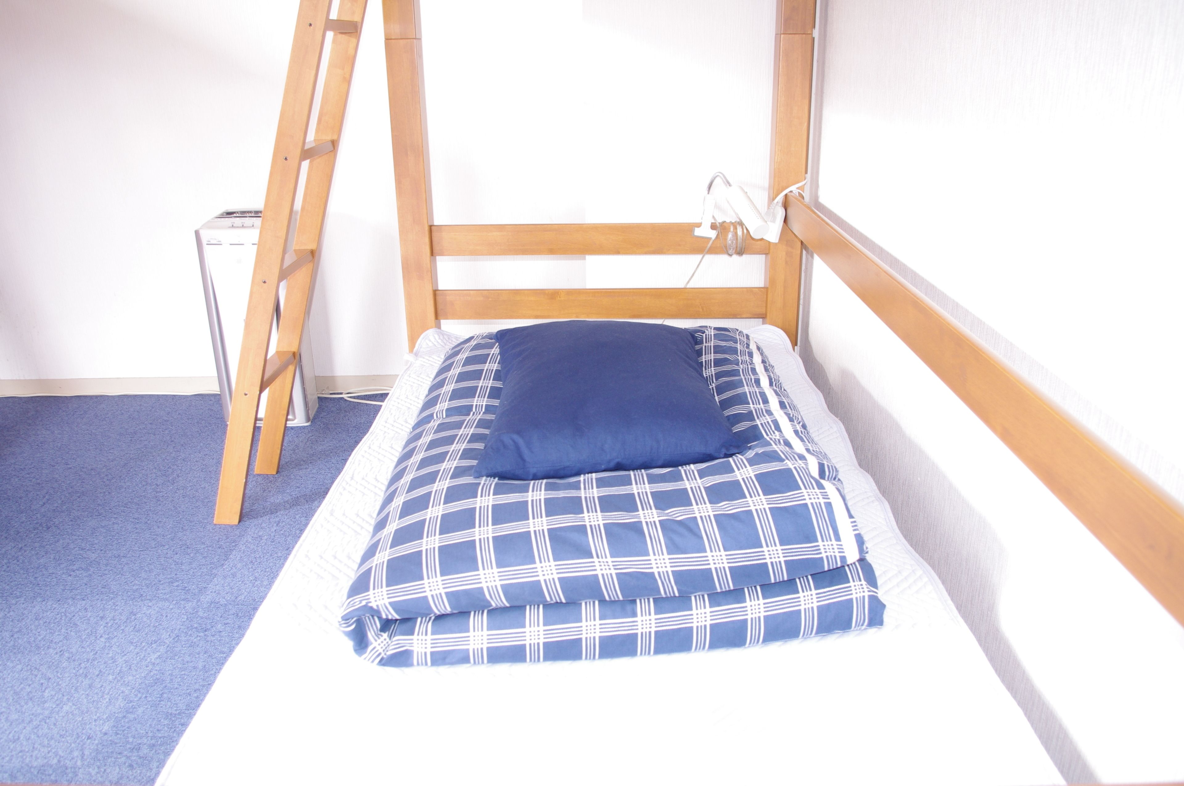 A small, single-bed room with a wooden headboard, a blue pillow, and a plaid blanket.