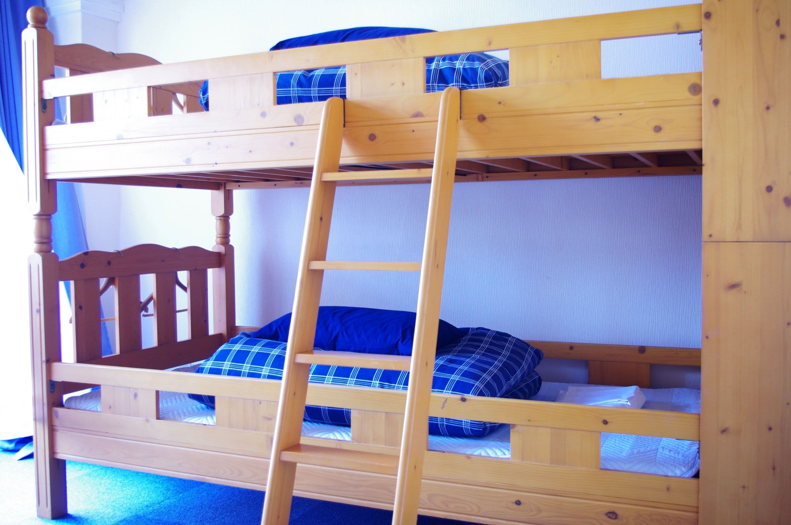 Una cama litera con escalera de madera, ropa de cama azul y cabecera de madera.