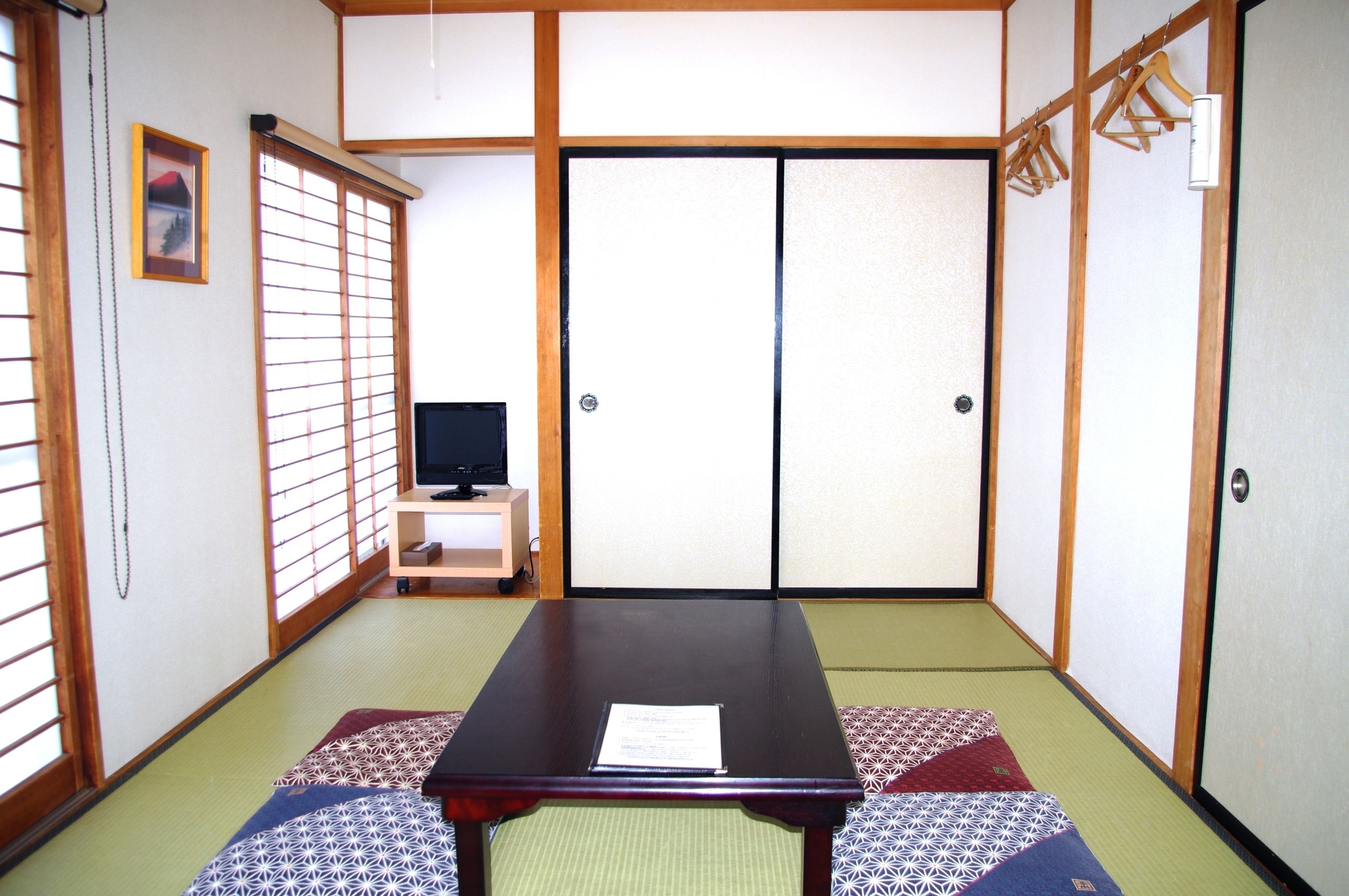 A traditional Japanese room with tatami flooring, a low table, a television, and sliding doors.