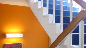 A staircase with wooden handrails and white steps, leading to a landing with a blue carpet and a wall-mounted light fixture. - K's House Mt.Fuji (Fujikawaguchiko)