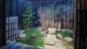 A wooden deck with a stone pathway, bamboo fence, and small trees.