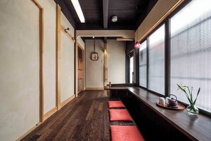 A narrow hallway with wooden flooring, a bench with cushions, a window with a view, and a small table with a teapot and cups. - Akane-an Machiya Holiday House (Kyoto)