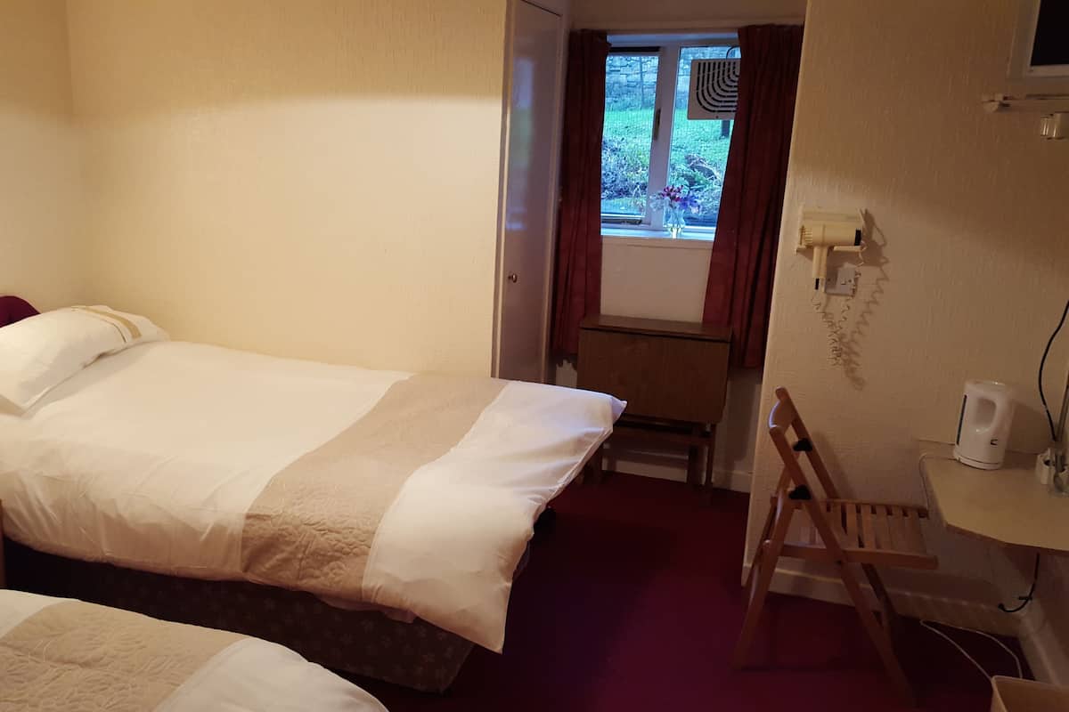 Ein Hotelzimmer mit einem Bett, einem Schreibtisch, einem Stuhl, einem kleinen Tisch und einem Fenster mit Vorhängen.