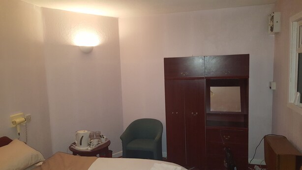 Une chambre d’hôtel comprenant un lit, un bureau avec une lampe, une chaise, une armoire et une table de chevet avec une bouilloire et des tasses.