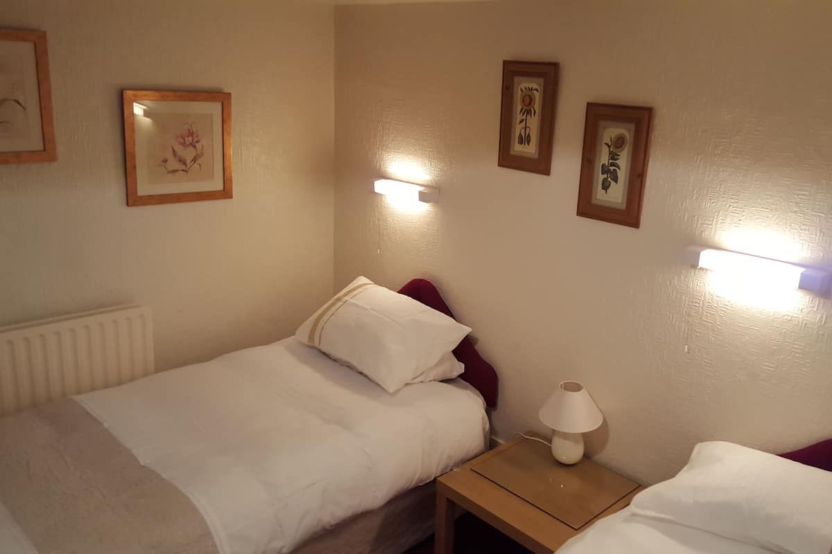 Ein Hotelzimmer mit zwei Betten, einem Nachttisch mit Lampe und drei gerahmten Bildern an der Wand.