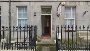Un bâtiment portant une enseigne indiquant « MAISON », une entrée fermée par un portail et un petit jardin.