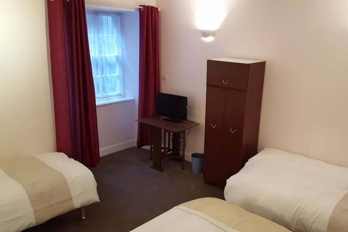 Ein Zimmer mit zwei Betten, einem Schreibtisch mit Computer, einem Kleiderschrank und einem Fenster mit Vorhängen.